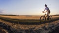 The cyclist rides a bike on the road near the field against the backdrop of the setting sun. Outdoor sports. Healthy lifestyle Royalty Free Stock Photo