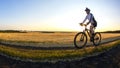 The cyclist rides a bike on the road near the field against the backdrop of the setting sun. Outdoor sports. Healthy lifestyle Royalty Free Stock Photo