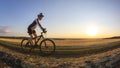 The cyclist rides a bike on the road near the field against the backdrop of the setting sun. Outdoor sports. Healthy lifestyle Royalty Free Stock Photo