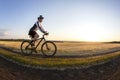 The cyclist rides a bike on the road near the field against the backdrop of the setting sun. Outdoor sports. Healthy lifestyle Royalty Free Stock Photo