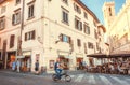 Cyclist riding past restaurants with eating people on street off the ancient Tuscany city
