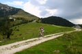 A cyclist on the road between the fields with view on the mountains and the houses in the clouds.