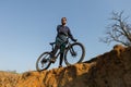 Cyclist in shorts and jersey on a modern carbon hardtail bike with an air suspension fork standing on a cliff against the backgrou