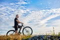 Cyclist standing with mountain bike on background of beautiful sky with clouds. Royalty Free Stock Photo