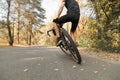 Cyclist tricks on bicycle on road in autumn forest, photo behind, focus on wheel. Man rides a bicycle ride on a country road in Royalty Free Stock Photo