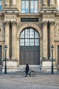 Cyclist walking in front the Pavillon Colbert of the Louvre museum, Paris, France