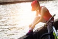 Cyclist woman tying shoeslace along the canal in sunset