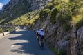 Cyclists cycling in shade on country road by mountain during sunny day