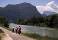 Cyclists on riverside bike way with mountain view.