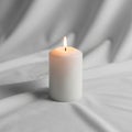 Cylindrical candle is lit, placed on a smooth, light gray fabric Royalty Free Stock Photo