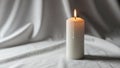 Cylindrical candle stands on a softly draped white fabric casting a Royalty Free Stock Photo