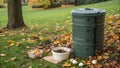 A cylindrical compost bin made from recycled plastic sits on a patch of grass partially covered by autumn leaves. The Royalty Free Stock Photo