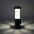 A cylindrical LED lantern emits a bright white light in a dark setting. It features a green Royalty Free Stock Photo