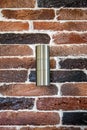 Cylindrical steel light fixture is fixed to an old brick wall. The colored bricks are varnished. Vintage decor.