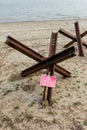 Czech anti tank hedgehoges and warning sign on river bank. Antitank obstacles on sand. Defensive war of Ukraine against Russian