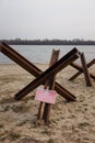 Czech anti tank hedgehogs and warning sign on river bank. Antitank obstacles on sand. Defensive war of Ukraine against Russian