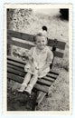 Vintage photo shows a small girl sits on a bench, circa 1943