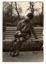 Vintage photo shows a young woman sit on a bench, circa 1960s