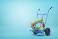 3d close-up rendering of big golden crown on blue hand truck on light-blue background.