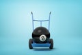3d close-up rendering of black bowling ball on blue hand truck on light-blue background.