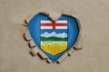 Heart shaped hole torn through paper, showing Alberta flag