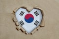 Heart shaped hole torn through paper, showing South Korean flag Royalty Free Stock Photo