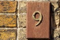 9 in brass on a simple wooden board on a yellow brick wall