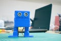 3D printed Funny dancing blue robot on the background of devices and laptop. Robot model printed on automatic three dimensional 3d