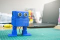 3D printed Funny dancing blue robot on the background of devices and laptop. Robot model printed on automatic three dimensional 3d