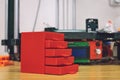 3D printed red plastic dresser on the background of three dimensional 3d printer. furniture model printed on automatic three