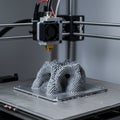 3D printer in action, crafting a complex gray structure with layered, arch-like patterns.