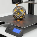 A 3D printer creating a geometric, hollow dodecahedron with illuminated orange core.