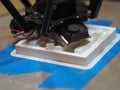 3D printer printing in white abs a texture over blue tape attached to the heat bed