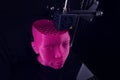 A 3D printer produces a futuristic sculptural humanoid head from pink plastic in foggy light.