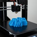 3D printer producing a complex, abstract blue object on its build platform.