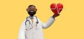 3d render. Doctor african cartoon character. Cardiologist shows red heart symbol. Clip art isolated on yellow background. Medical Royalty Free Stock Photo