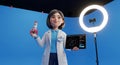 a 3d rendered cartoon of a female scientist presenting space exploration with a rocket, tablet, and ring light against a blue back Royalty Free Stock Photo