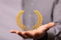 3D rendered gold laurel wreath icon on a person's hand - a concept of achievement