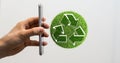 3D rendered green recycle sign in front of a hand holding a smartphone