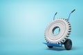 3d rendering of big grey wheel gear on blue hand truck which is standing in half-turn on light-blue background with much