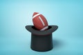 3d rendering of black tophat upside down with brown gridiron football inside on light blue background.