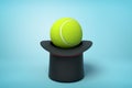 3d rendering of black tophat upside down with tennis ball inside on light-blue background.