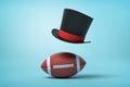 3d rendering of a brown gridiron football and a black tophat floating in air above the ball on light blue background. Royalty Free Stock Photo