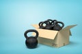 3d rendering of cardboard box full of several black kettlebells on blue background.