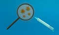 3D rendering of coronaviruses with a syringe seen under a magnifying glass on a blue background