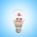 3d rendering of lightbulb with sand, two chaise-longues and beach umbrella inside, on light-blue background.