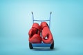 3d rendering of pair of big red boxing gloves on blue hand truck standing in half-turn on light-blue background with Royalty Free Stock Photo