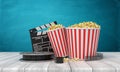 3d rendering of pop corn bucket, film reel, and clapperboard standing on wooden floor near blue wall.