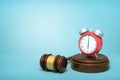3d rendering of red alarm clock standing on sounding block with judge gavel lying beside on light-blue background.