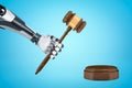 3d rendering of robotic hand holding brown wooden gavel with round wooden block on blue background